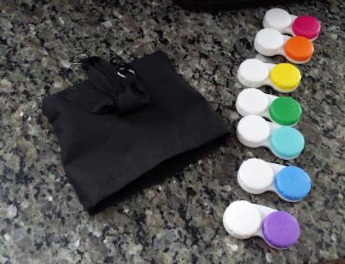 little black satchel, open and empty, rainbow colored contact lens containers lined up next to it