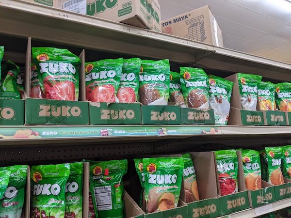 a set of shelves in a Mexican grocery store, covered in different flavors of a sugary powdered drink mix called Zuko
