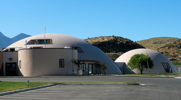 Photo of two white concrete domes with windows and doors, from https://en.wikipedia.org/ wiki/ Monolithic_dome#/media/File:Domes--Genola,Utah