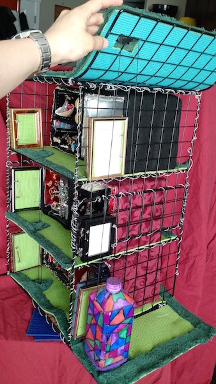 Another still photo of half-scale model of 6 apartment cubes on 3 stories of wire shelving. This one is also centered on the elevator, showing how the strings that control it go up into an opening in the up-slanted side of the roof, and then loop back down through holes in the walkways.