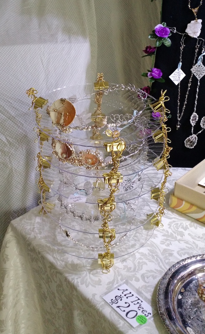 Close-up of the stack of plates holding up crowns. In this version the plates are clear, not turquoise. Each is supported by four gold-wire columns, making the plates into shelves on which the crowns sit. The crowns visible in this image are made of steel wire and decorated with seashells and pearls. 